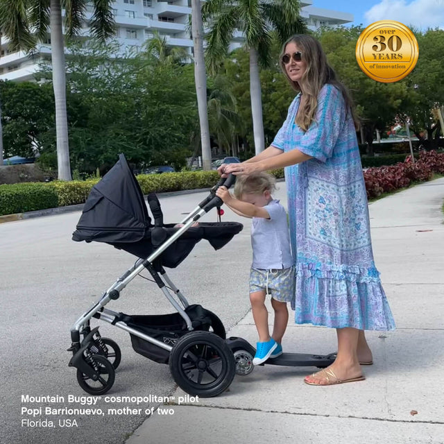 mother of two pushing cosmopolitan pram in parent facing position with freerider™ scooter attached - Mountain Buggy cosmopolitan™ pilot Popi Barrionuevo, Florida, USA - fabric colour_black