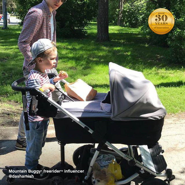family strolling through park with toddler riding their freerider™ scooter board attached to rear of duet™ double pram - Mountain Buggy freerider™ influencer @dashamish